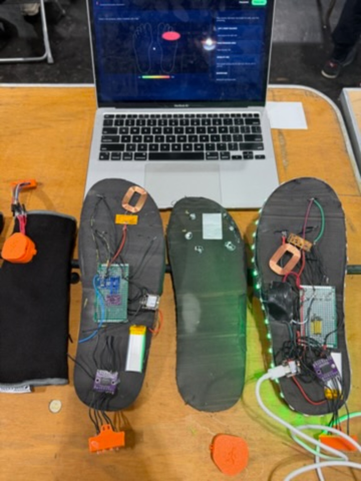 Three instrumented insoles with their electronics, and the laptop software interface behind them.