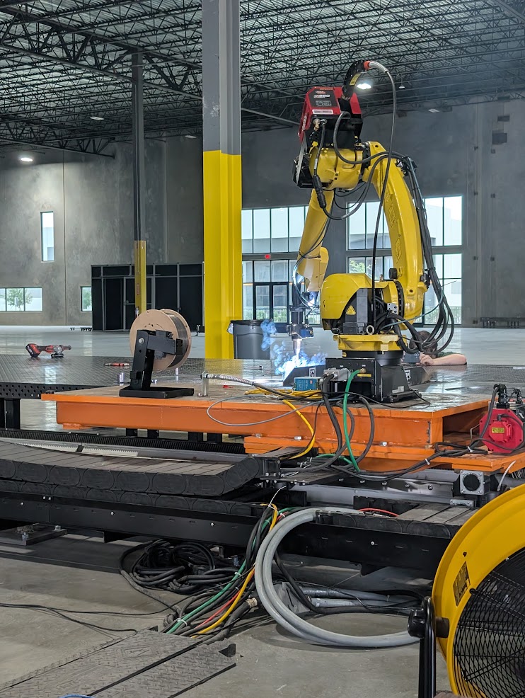 One of the FANUC robots welding a part on the fixture, with the cable carrier and carriage below it.